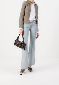 Osoba ubrana w jasnoszare dżinsy, taupe kurtkę na białą koszulę, metaliczne, spiczaste buty, trzyma małą ciemnobrązową skórzaną torebkę.