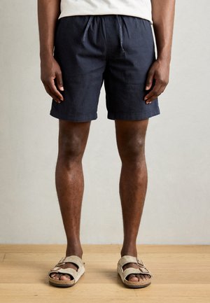 Navy blue shorts made of lightweight fabric, featuring an elastic waistband with drawstring, and a relaxed fit. Sandals with two straps.