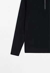 Pull noir côtelé à manches longues avec une fermeture éclair partielle à l'avant et un ourlet droit sur fond blanc.
