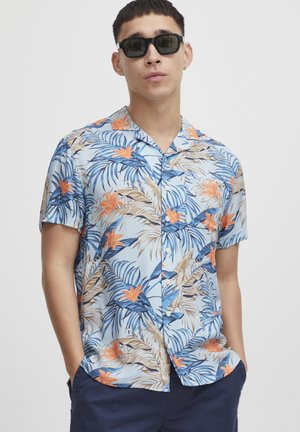 Kortermet, skjortebluse med knapper i lyseblått stoff. Har et tropisk blomsterdesign med oransje blomster og grønne blader. Slank tekstur.