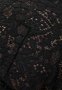 Schwarzer Spitzenstoff mit floralen Motiven, der erhabene Texturen und ein kompliziertes Muster mit offenen Geweben und festen Bereichen aufweist, was Tiefe und Kontrast erzeugt.