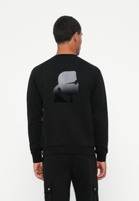 Felpa nera con polsini e orlo a costine, presenta una grafica silhouette a gradiente grigia sul retro. Texture liscia, design classico a collo rotondo.