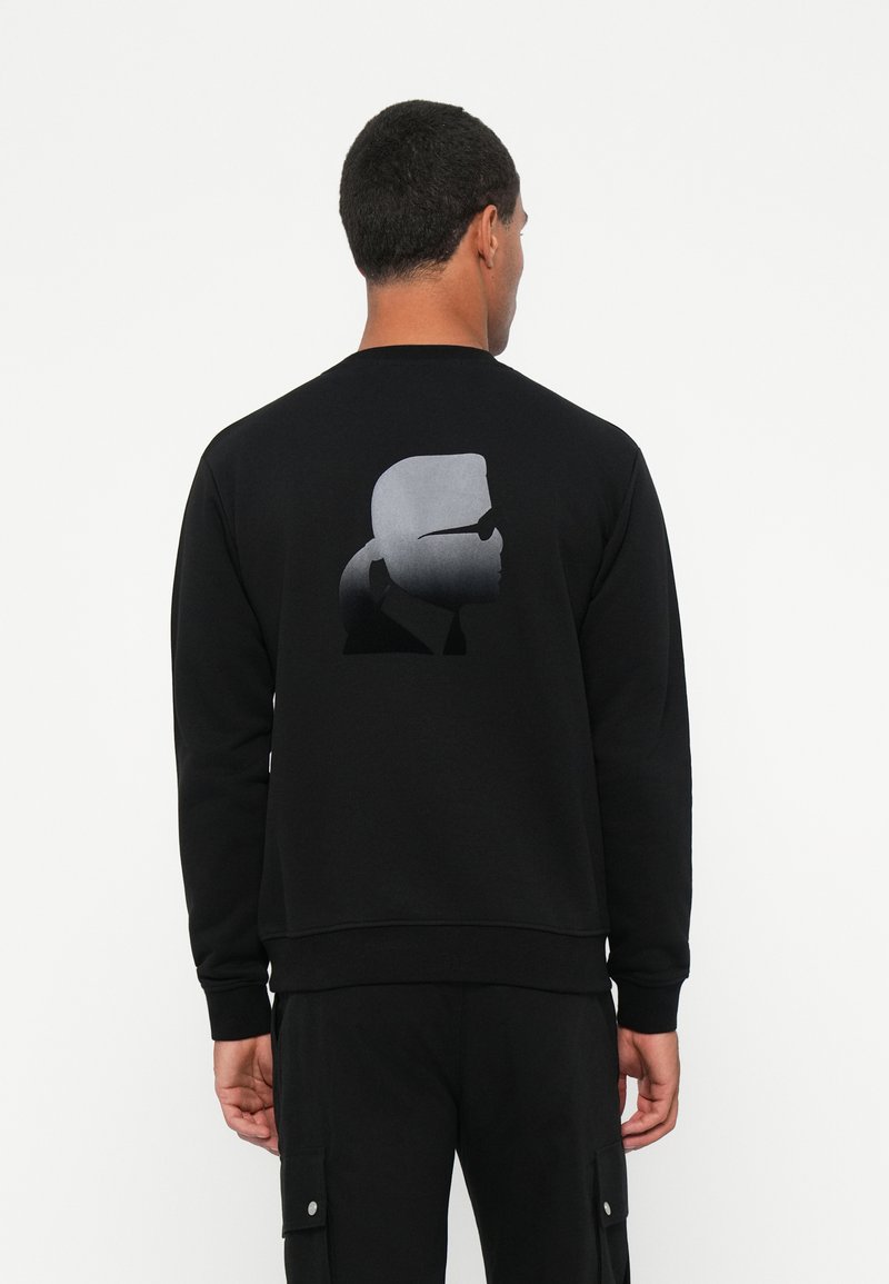 Felpa nera con polsini e orlo a costine, presenta una grafica silhouette a gradiente grigia sul retro. Texture liscia, design classico a collo rotondo.