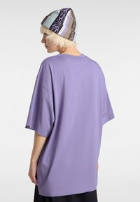 T-shirt oversize viola con maniche corte, tessuto di cotone morbido e scollatura tonda. Indossato con un berretto di maglia multicolore.