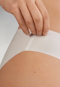 Weiße nahtlose Unterwäsche, die gerade angepasst wird. Der Stoff ist glatt mit einem leichten Glanz, verfügt über einen weichen elastischen Bund und keine sichtbaren Nähte.