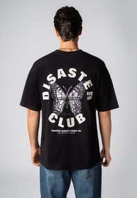 Schwarzes Baumwoll-T-Shirt mit einem großen lila-weißen Schmetterlingsmotiv auf der Rückseite, darunter der Schriftzug "DISASTER CLUB" und ein Slogan.