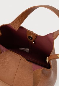 Sac à main en cuir marron texturé avec une large bandoulière, ouvert montrant une doublure intérieure bordeaux et une fermeture à pression magnétique.