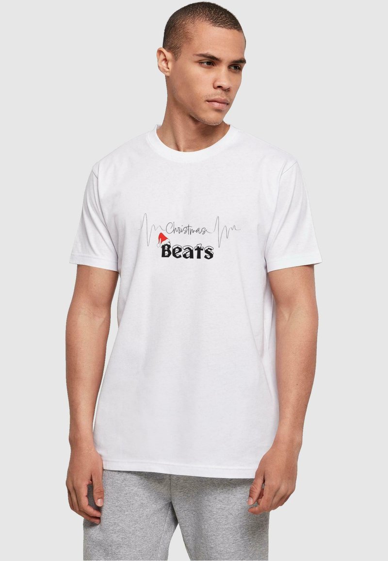 Camiseta de algodón blanca con un gráfico de "Christmas Beats" en negro y rojo, con un patrón de onda sonora encima del texto. Manga corta y cuello redondo.