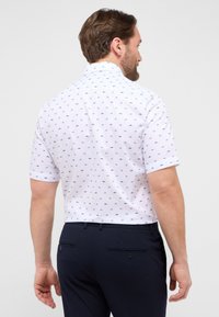 Korte mouwen polo shirt in het wit met blauwe micro-patronen. Beschikt over een kraag en een gladde textuur, gecombineerd met donkerblauwe broeken.