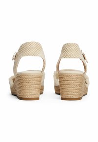 Sandali con zeppa con cinturini intrecciati di colore crema e tacchi in juta beige texturizzati. Cinturino alla caviglia regolabile. Design con retro aperto.