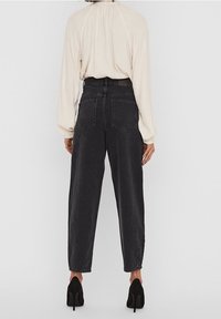 Högmidjade svarta jeans med en avslappnad passform, med två bakfickor, stiliserade sömmar och en mjuk textur. Bärs med en krämfärgad blus.