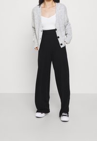 Gray knit cardigan with buttons, worn over a white top, paired with high-waisted black wide-leg pants and white sneakers.