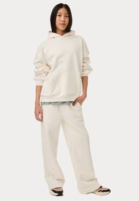 Crème-kleurige hoodie met een voorzak, gecombineerd met een losse, bijpassende crème broek. Beide gemaakt van zachte stof.