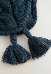 Stickad mörk tealtyg med flätad finish, som har två stora tofsar i ändarna, vilket framhäver struktur och rik färg.