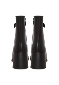 Para czarnych skórzanych botków za kostkę na słupkowych obcasach, widocznych od tyłu na białym tle.