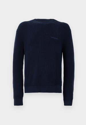 Suéter azul marino con un patrón de punto texturizado, cuello redondo acanalado y puños. Presenta un pequeño logotipo en el lado izquierdo.