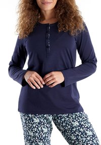 Navy langemouwen top met een knoopsluiting; gecombineerd met pyjamabroek met bloemenpatroon in tinten blauw en wit op een donkere achtergrond.