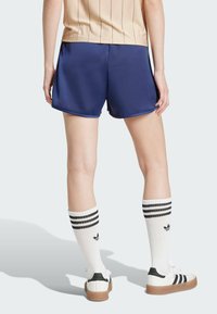 Mornarske atletske kratke hlače s glatkom teksturom, zaobljenim rubom, u kombinaciji s bijelim čarapama do koljena s crnim prugama i ležernim tenisicama.