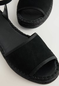 Zwarte suède espadrille sandalen met open teen, platte geweven jute zool en stoffen banden. Matte afwerking zonder decoratieve patronen.