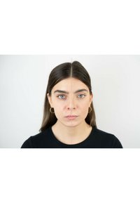 Primo piano di una donna con capelli castani di lunghezza media e occhi verdi, che indossa orecchini a cerchio dorati e una maglietta nera. Vista simmetrica in due parti.