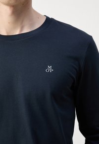 Marine langærmet t-shirt lavet af blød bomuld. Har en rund hals og et lille hvidt "MOP" logo på brystet. Glat tekstur, tætsiddende design.