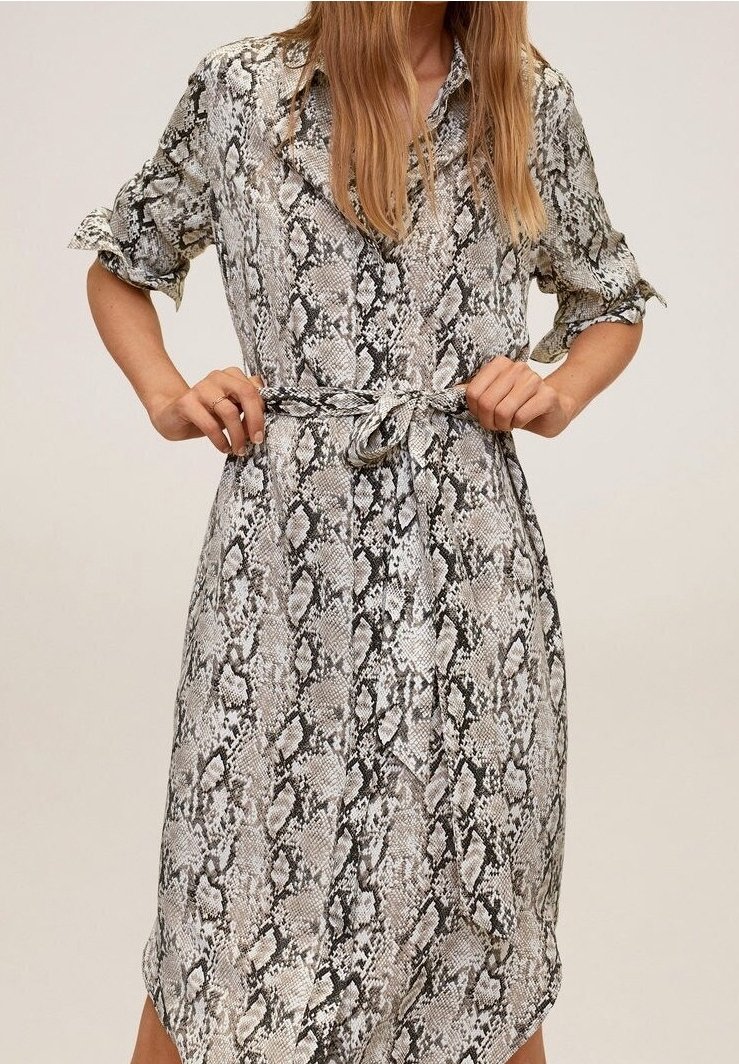 Femme nouant une ceinture sur une robe à boutons arrivant au genou, avec des manches retroussées et un motif en peau de serpent gris, noir et beige.