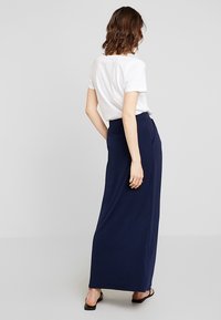 Tmavě modrá maxi sukně s pružným pasem, splývavým designem a hladkou texturou. Slaďte s bílým tričkem s krátkým rukávem.