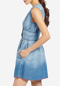 Jasnoniebieska sukienka dżinsowa bez rękawów, ze wcięciem w talii, bocznymi kieszeniami i subtelnym gradientem u dołu. Charakteryzuje się gładką teksturą i zapięciem z tyłu.