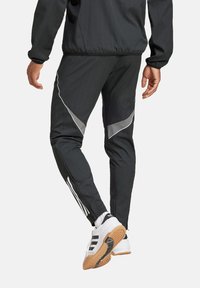 Schwarze Sporthosen mit schlanker Passform, ausgestattet mit reflektierenden Akzenten, grauen Seitenpaneelen und weißen Streifen entlang des äußeren Beins.