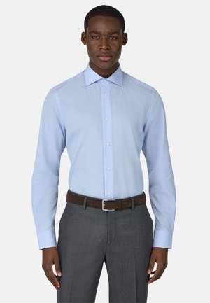 Camicia a quadri azzurri chiari con colletto button-down e maniche lunghe. Abbinata a pantaloni grigi e a una cintura marrone. Tessuto di una consistenza liscia.