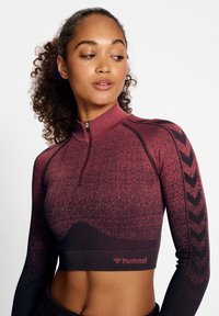 Tiefburgunderfarbenes, langärmeliges Sportoberteil mit einem Viertel-Reißverschluss, texturiertem Muster und schwarzen Chevronakzenten. Besitzt ein tailliertes, kurzes Design.