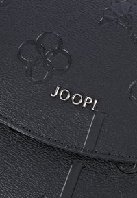 Sezione della borsa in pelle nera texture, impreziosita da motivi floreali in rilievo e lettere in metallo argentato che formano la scritta "JOOP!".