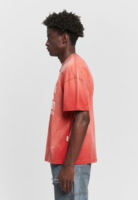 T-shirt rouge dégradé à manches courtes, avec une grande inscription blanche à l'avant. Coupe décontractée avec un ourlet légèrement effiloché.