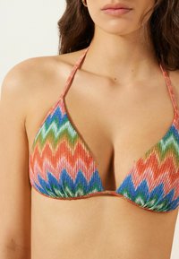 Trojúhelníkový bikini top s živým cikcakovým vzorem v červené, modré, zelené a oranžové barvě. Texturovaná tkanina s zavazováním za krk.