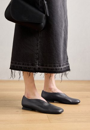 Mustad nahast laudlinad, millel on V-kujuline lõige ja madal konts, koos tumeda denimsiidiga seelikuga, millel on rebenenud servad ja tekstuuritunne.