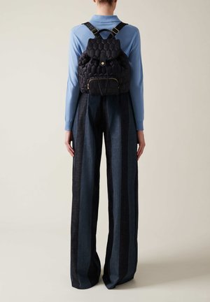 Zaino trapuntato nero con parte superiore arrotondata, zip dorata e spallacci in tessuto. Abbinato a pantaloni a gamba larga con righe verticali blu.