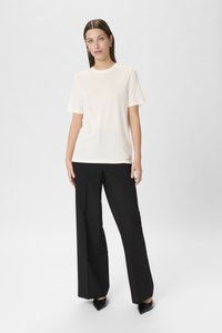 Hvid, kortærmet t-shirt parret med højhalsede, vide sorte bukser. Outfittet har en glat tekstur og et minimalt design.