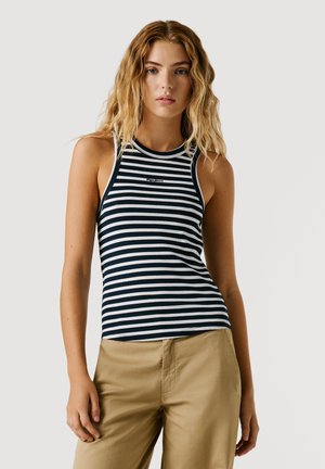 Marineblaue und weiße gestreifte ärmellose Bluse mit gerippter Struktur und hohem Kragen, versehen mit einem kleinen Logo in der Mitte. Kombiniert mit khakifarbenen Hosen.