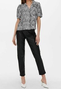 Blouse à manches courtes à motifs noir et blanc avec un décolleté en V, associée à un pantalon en cuir noir ajusté et des chaussures à talons hauts blanches.