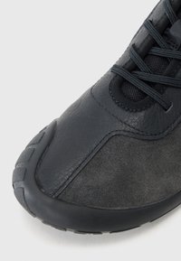 Baskets noires comprenant un mélange de cuir texturé et de matériau lisse. Bout arrondi et semelle en caoutchouc plate avec un motif de treads détaillé.