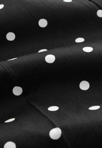 Tissu noir à pois blancs régulièrement espacés, montré en gros plan avec une texture visible et des plis doux.