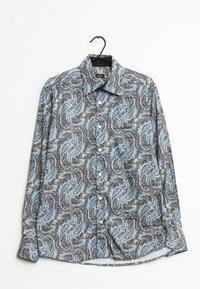 Långärmad skjorta med knappar i blå, svart och vit paisleymönster som hänger på en svart galge mot vit bakgrund.