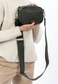 Ciemnzieleńska skórzana torba na ramię o prostokątnym kształcie, teksturowanej powierzchni, srebrnych elementach i regulowanym pasku. Logo nadrukowane na przodzie.