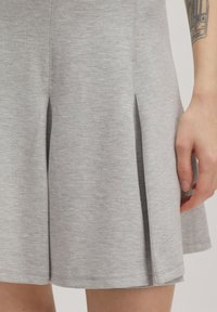 Grau, weich strukturierter Kleid mit ausgestelltem Design und zwei seitlichen Schlitzen, glatter Oberfläche und kontrastierendem dunklem Stoff in den Schlitzen.