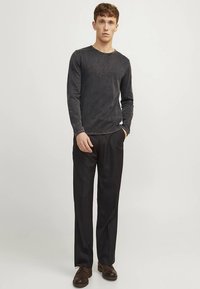 Donkergrijs shirt met lange mouwen en een ronde halslijn, gecombineerd met zwarte broek en donkere schoenen. Gladde stof met subtiele textuur.