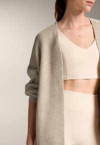 Svetlo béžový rebrovaný cardigan s dlhými rukávmi, nosený cez zodpovedajúci krčný crop top. Mäkko textúrovaný, otvorený predok a voľný strih.