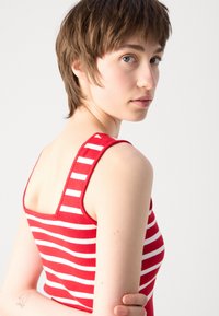 Débardeur à rayures rouges et blanches avec de larges bretelles et un col carré. Tissu tricoté, design ajusté et detailing minimal.
