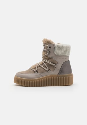 Bottes montantes grises et beige avec une semelle en caoutchouc texturée, dotées de laçage à l'avant, d'un col en tricot et d'un doublure en peluche.