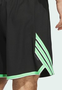 Svarta sportshorts med gröna och vita accenter, med nätpaneler och en logotyp, skräddarsydd passform och knälång design.