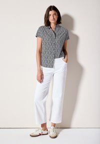 Camicia a maniche corte con bottoni, con un motivo a foglie in bianco e nero, abbinata a pantaloni bianchi a gamba larga e sneakers beige e rosse.